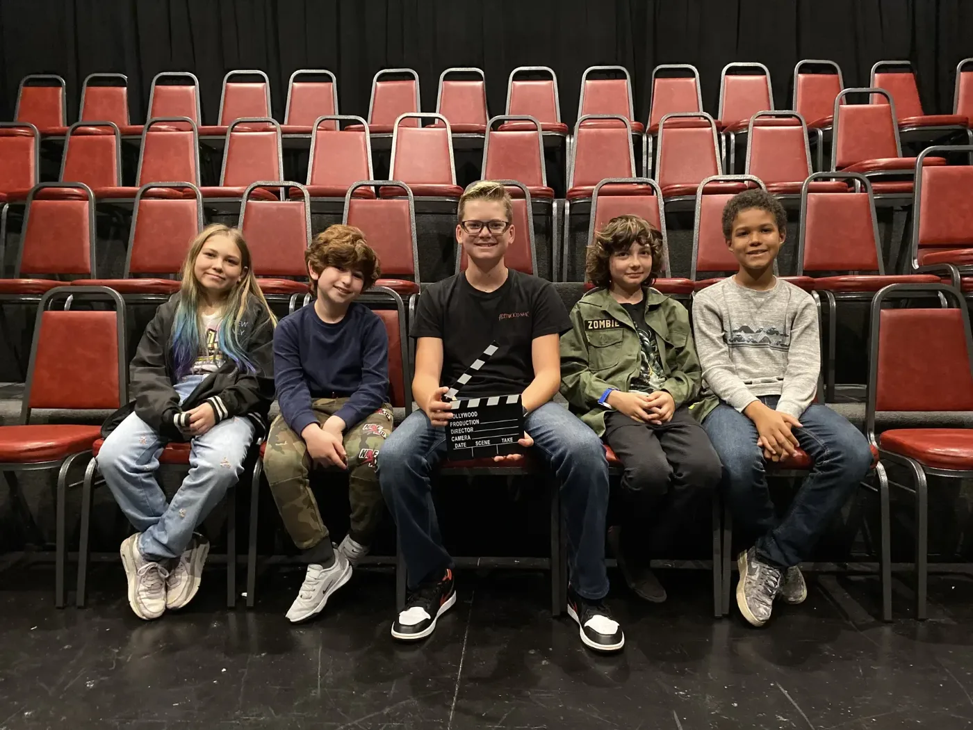 Film camp kids in the theatre seats with a clapperboard, waiting for their film to screen