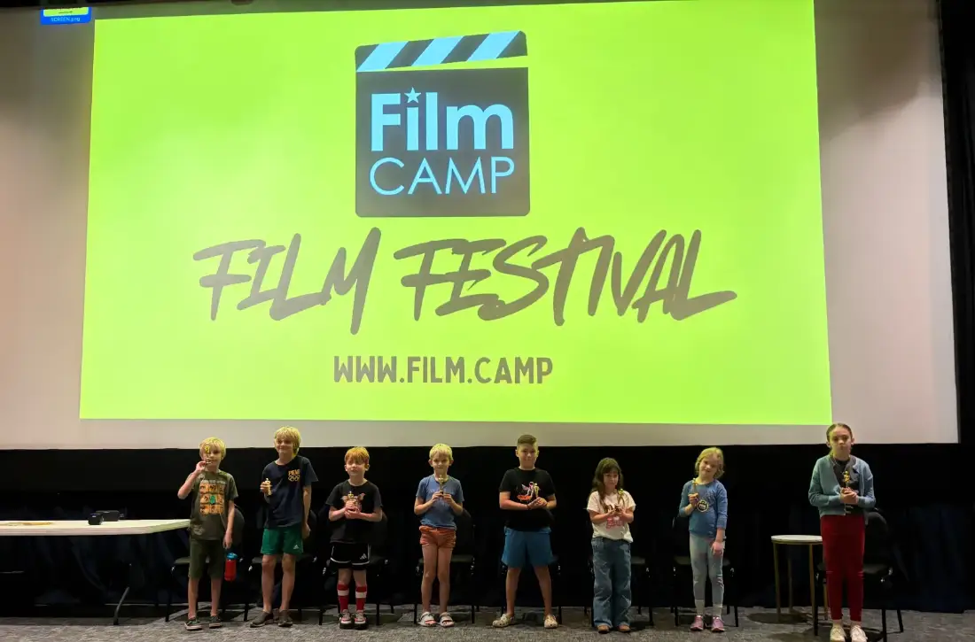 A film camp crew of kids shooting a scene with a professional video camera